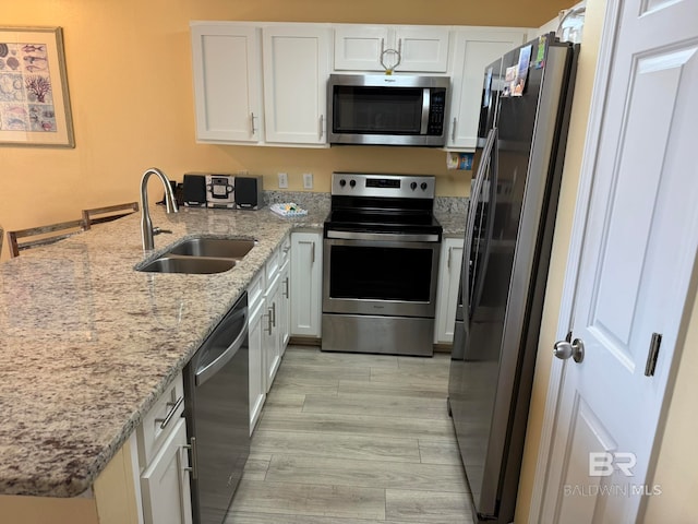 kitchen with appliances with stainless steel finishes, sink, white cabinets, light stone counters, and light hardwood / wood-style flooring