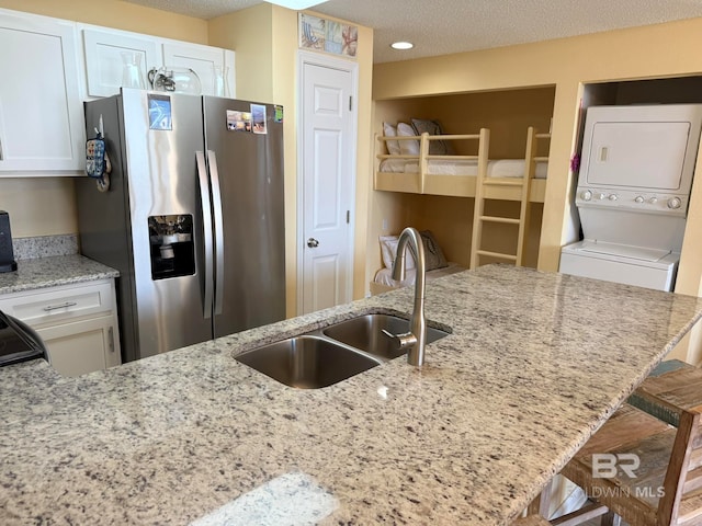 kitchen featuring stainless steel fridge, white cabinets, stacked washer and clothes dryer, and a breakfast bar