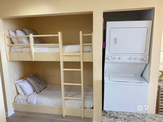 unfurnished bedroom featuring stacked washer / drying machine and hardwood / wood-style flooring