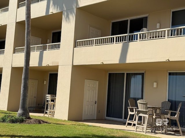 rear view of property featuring a balcony, a yard, and a patio