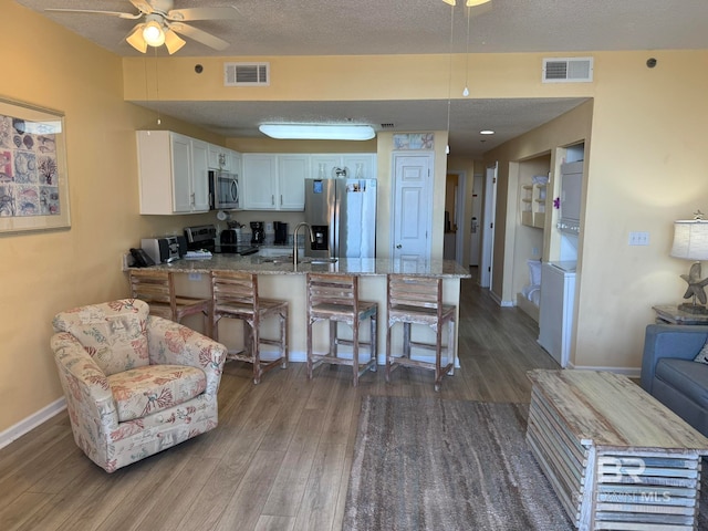 kitchen with stainless steel appliances, white cabinets, light stone counters, a breakfast bar, and dark hardwood / wood-style floors