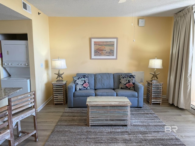 living room with stacked washing maching and dryer, a textured ceiling, and wood-type flooring