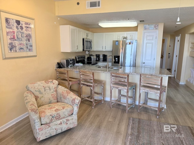 kitchen featuring appliances with stainless steel finishes, sink, light wood-type flooring, a kitchen breakfast bar, and white cabinets