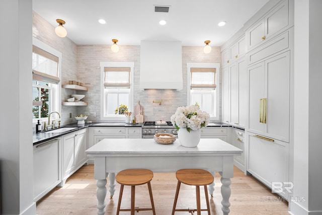 kitchen with custom exhaust hood, sink, stainless steel range oven, light wood-type flooring, and a kitchen bar