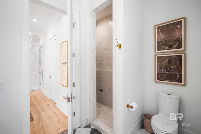 bathroom with a tile shower, crown molding, hardwood / wood-style flooring, and toilet