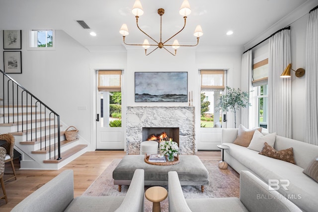 living room featuring crown molding, light hardwood / wood-style floors, a premium fireplace, and a notable chandelier