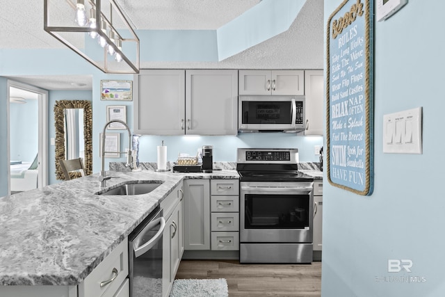 kitchen featuring sink, wood-type flooring, a textured ceiling, appliances with stainless steel finishes, and light stone countertops