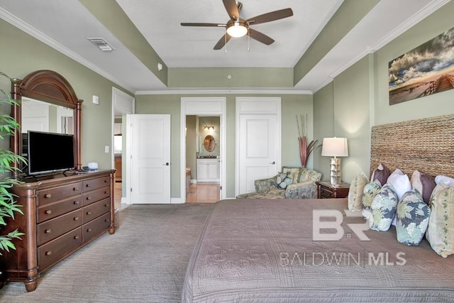 bedroom featuring ensuite bathroom, ceiling fan, ornamental molding, a tray ceiling, and light colored carpet