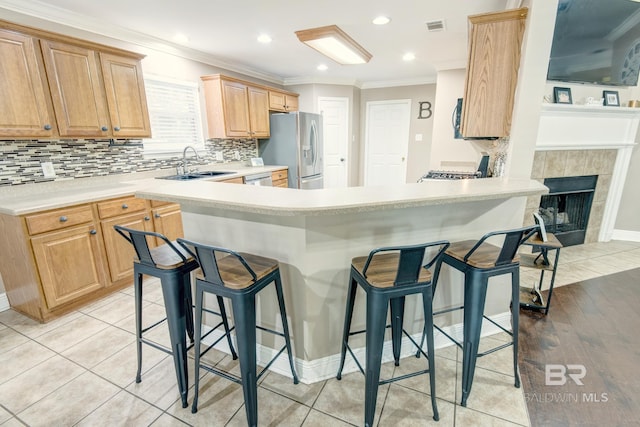 kitchen featuring stainless steel refrigerator with ice dispenser, sink, a breakfast bar, a tile fireplace, and light tile patterned floors