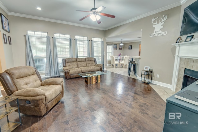 living room with hardwood / wood-style flooring, a tiled fireplace, crown molding, and ceiling fan