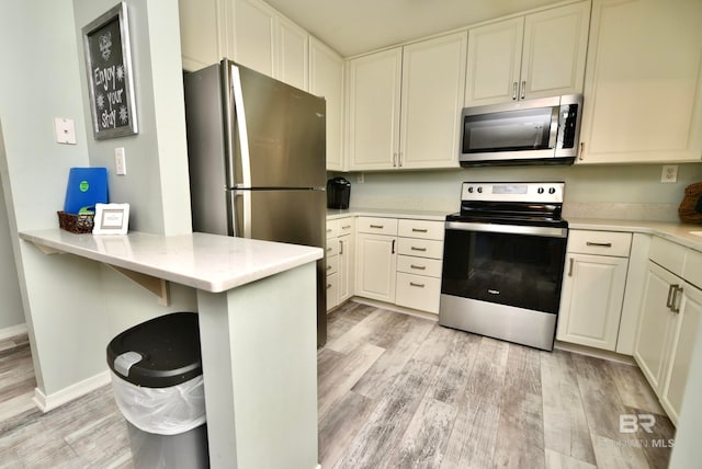 kitchen featuring appliances with stainless steel finishes, light stone counters, kitchen peninsula, and light hardwood / wood-style flooring