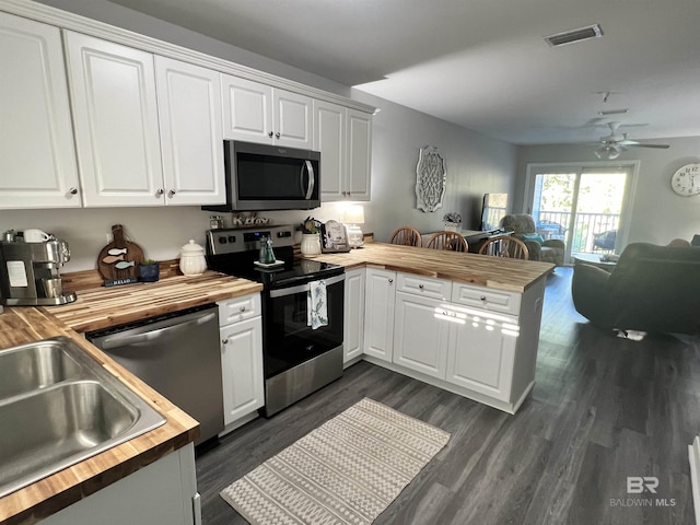 kitchen featuring stainless steel appliances, a peninsula, wood counters, visible vents, and open floor plan