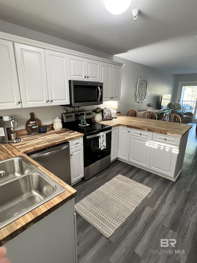 kitchen with a peninsula, stainless steel appliances, white cabinetry, wooden counters, and dark wood finished floors