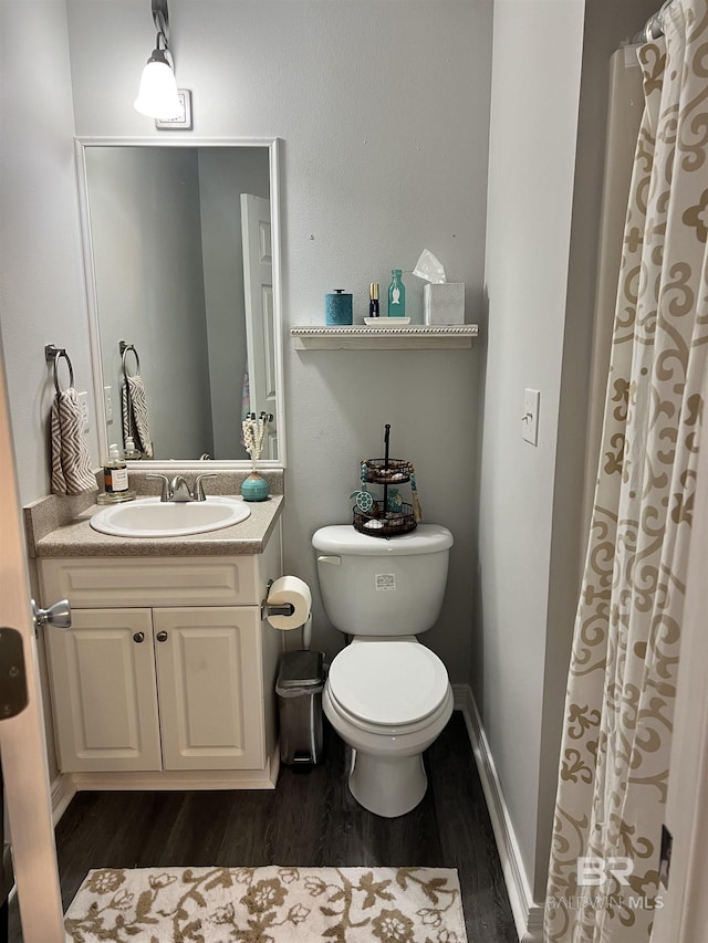 bathroom featuring toilet, baseboards, wood finished floors, and vanity