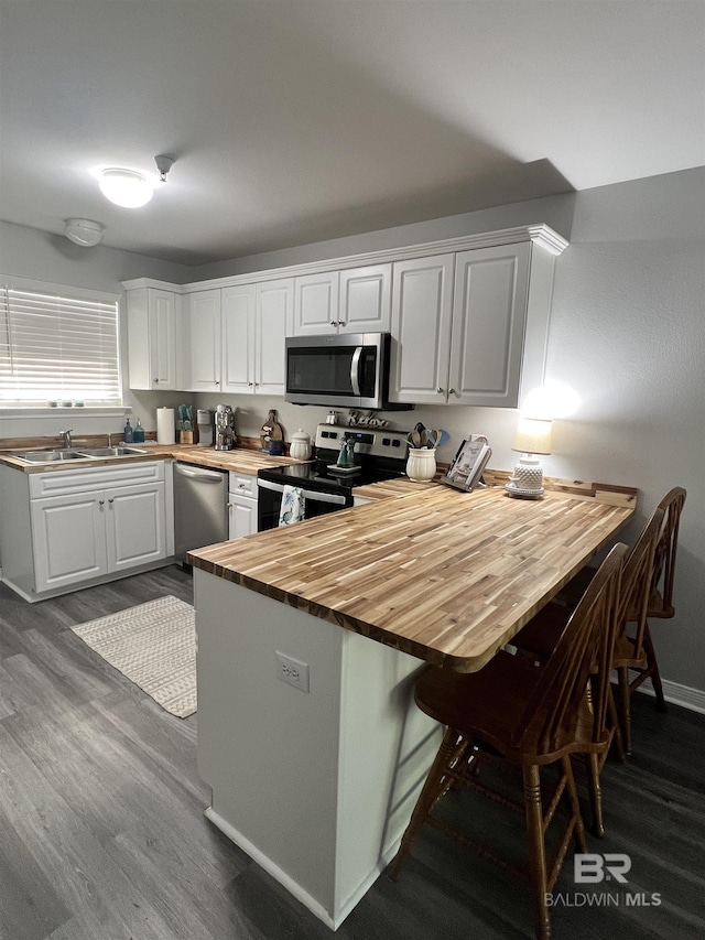 kitchen with a breakfast bar, dark wood-style flooring, white cabinets, wooden counters, and appliances with stainless steel finishes