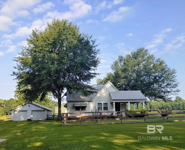 exterior space featuring a detached garage, fence, a lawn, metal roof, and an outbuilding