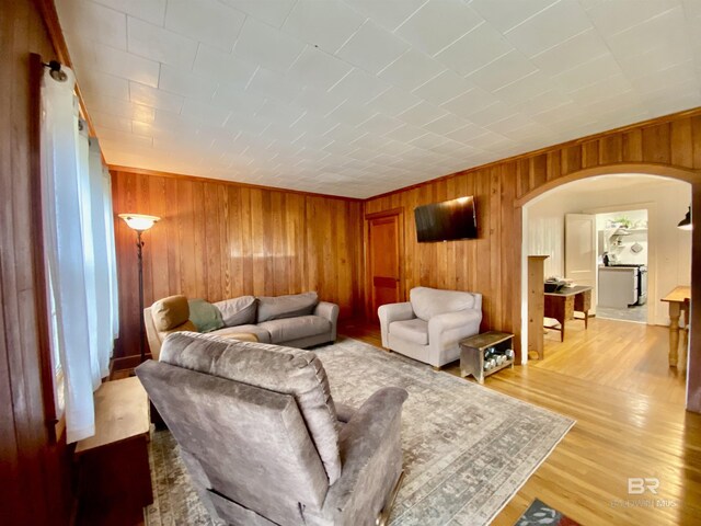 living area with arched walkways, wood walls, and light wood-type flooring