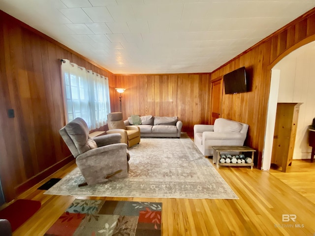 living area featuring visible vents, arched walkways, light wood-style floors, and wooden walls