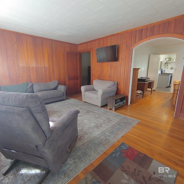 living room featuring arched walkways, wood finished floors, crown molding, and wood walls