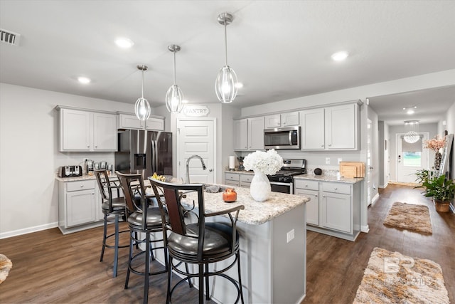 kitchen with an island with sink, dark hardwood / wood-style floors, sink, hanging light fixtures, and appliances with stainless steel finishes