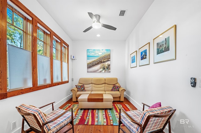 living area with a ceiling fan, wood finished floors, visible vents, and baseboards