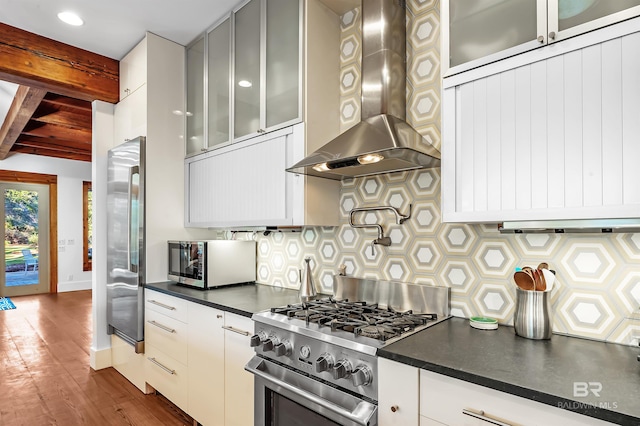 kitchen featuring beam ceiling, stainless steel appliances, dark countertops, tasteful backsplash, and extractor fan