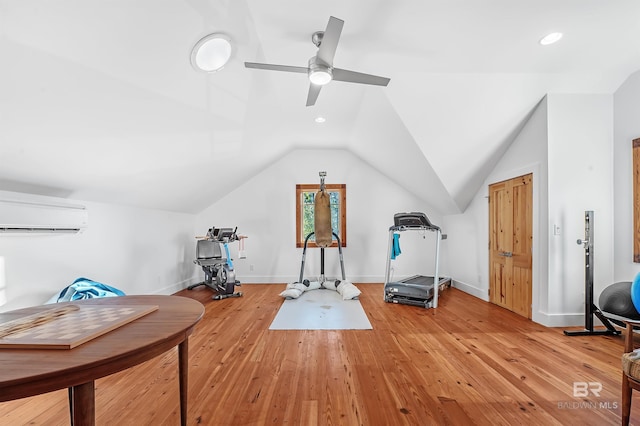 exercise room with lofted ceiling, a wall unit AC, baseboards, and light wood-style floors