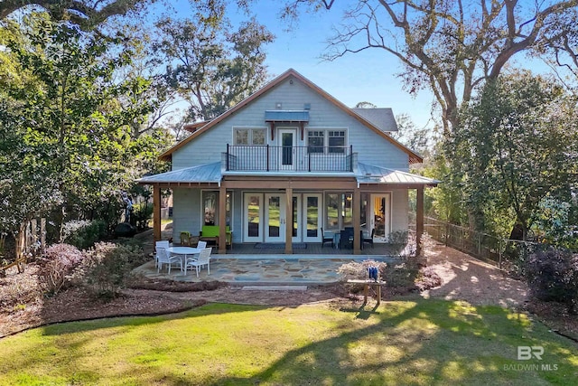 back of property featuring a balcony, metal roof, a standing seam roof, fence, and a yard