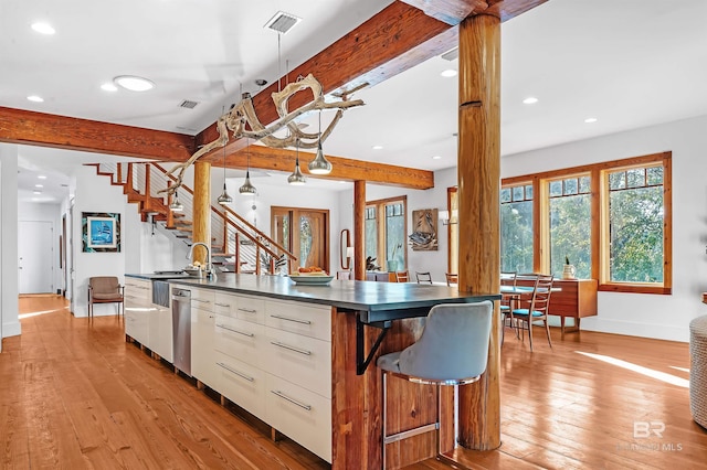 kitchen featuring visible vents, dark countertops, an island with sink, beamed ceiling, and light wood-style floors