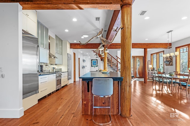 kitchen with high end appliances, dark countertops, beam ceiling, and light wood finished floors