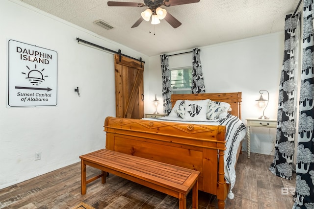 bedroom featuring dark wood-type flooring, a textured ceiling, ceiling fan, and a barn door