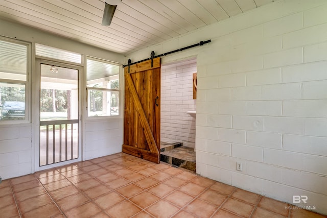 unfurnished sunroom with a barn door, ceiling fan, and a wealth of natural light