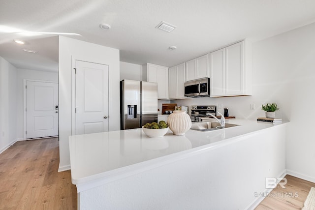 kitchen with a peninsula, white cabinets, light countertops, appliances with stainless steel finishes, and light wood finished floors