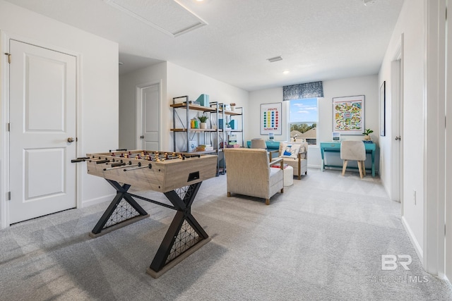 recreation room with attic access, light carpet, a textured ceiling, and baseboards