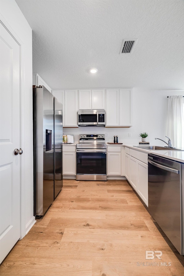 kitchen featuring stainless steel appliances, white cabinets, light countertops, and visible vents