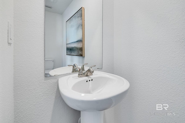 bathroom with toilet, a sink, and a textured wall