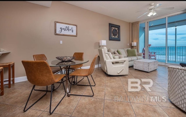 tiled dining room featuring ceiling fan, a wall of windows, and a water view