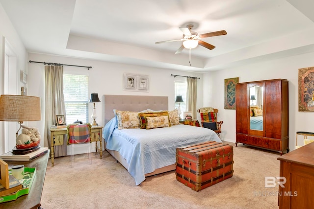 carpeted bedroom featuring multiple windows, a raised ceiling, and ceiling fan