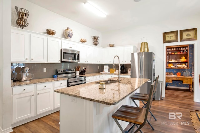 kitchen featuring appliances with stainless steel finishes, white cabinets, dark wood-type flooring, and an island with sink