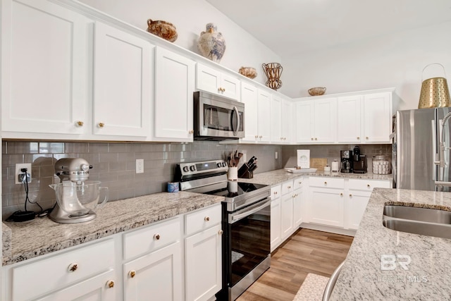 kitchen featuring decorative backsplash, white cabinets, light stone countertops, light hardwood / wood-style floors, and stainless steel appliances