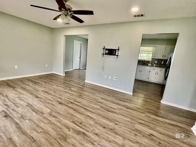 unfurnished living room featuring ceiling fan, light hardwood / wood-style flooring, and a textured ceiling