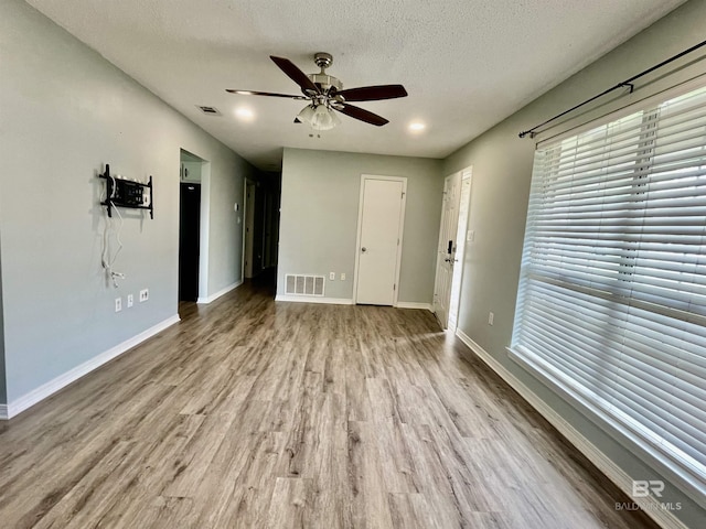 empty room with ceiling fan, a textured ceiling, and light wood-type flooring