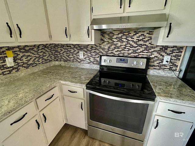 kitchen with dark wood-type flooring, wall chimney exhaust hood, light stone counters, stainless steel electric stove, and backsplash