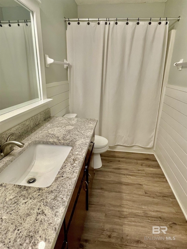 full bathroom featuring hardwood / wood-style flooring, shower / tub combo with curtain, vanity, and toilet