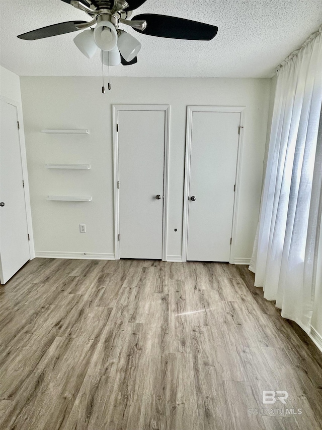 unfurnished bedroom with ceiling fan, light hardwood / wood-style floors, a textured ceiling, and two closets