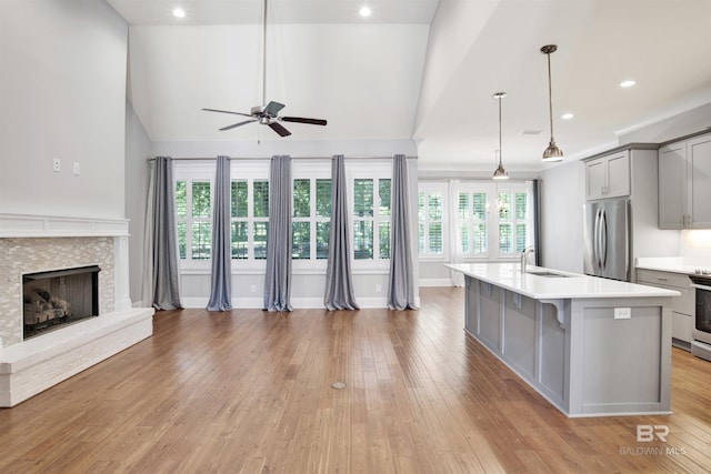 kitchen featuring gray cabinetry, stainless steel appliances, decorative light fixtures, a stone fireplace, and an island with sink