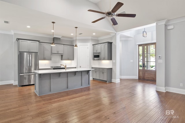 kitchen featuring gray cabinetry, a kitchen island with sink, decorative backsplash, stainless steel fridge, and built in microwave