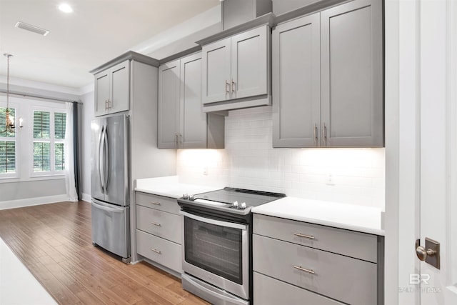 kitchen featuring light wood-type flooring, ornamental molding, gray cabinetry, stainless steel appliances, and hanging light fixtures