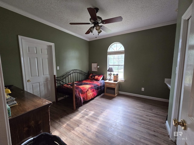 bedroom featuring a textured ceiling, ceiling fan, baseboards, ornamental molding, and wood finished floors