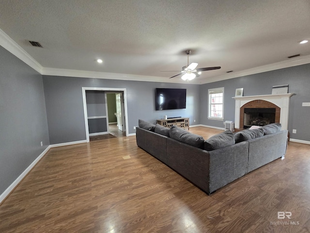living room with ceiling fan, crown molding, visible vents, baseboards, and wood finished floors